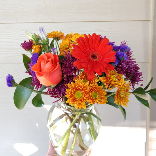 Mixed flower arrangement with flowers like daisies, roses, statice, gerbera, and greenery