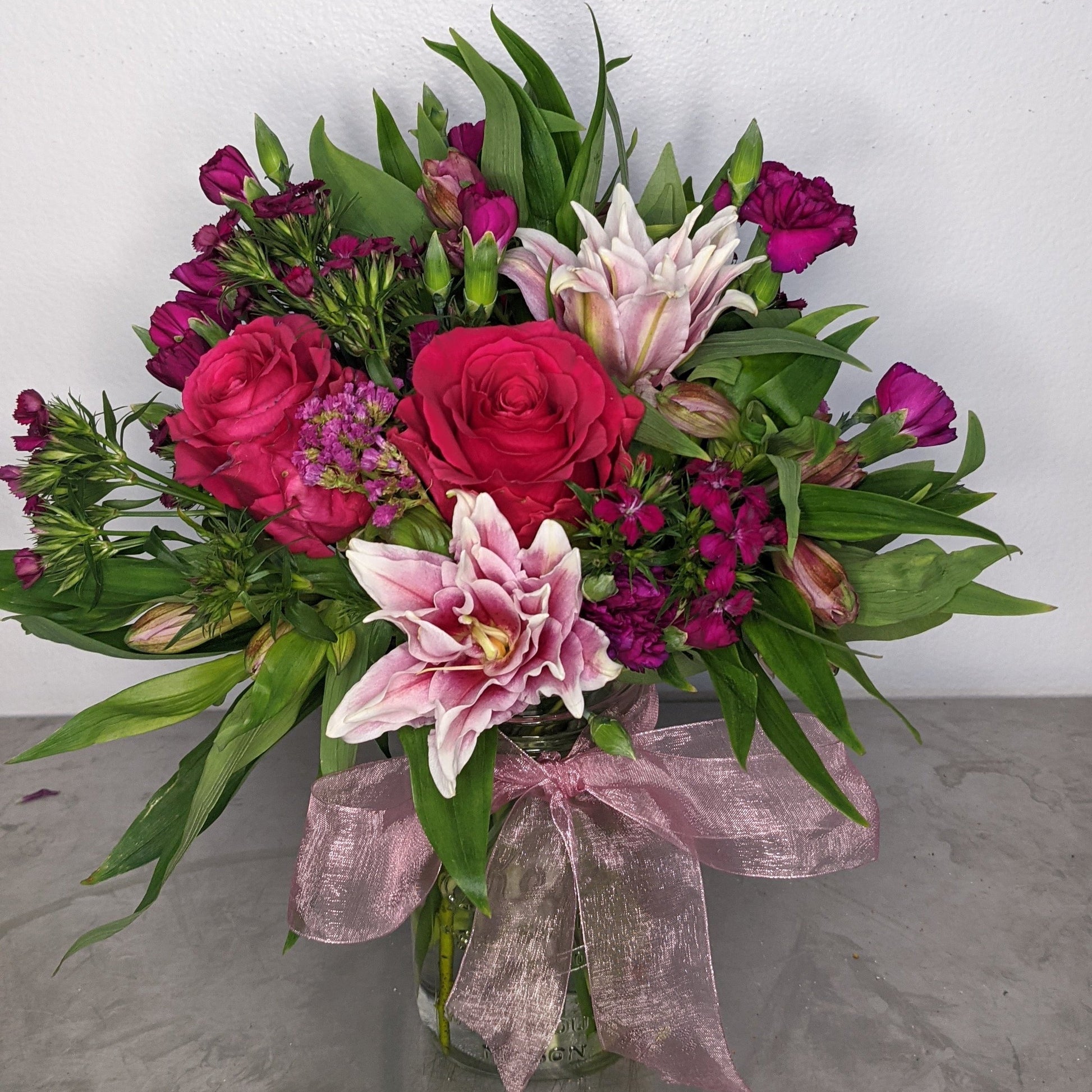 A beautifully elegant bouquet featuring stargazer or rubrum lilies as a focal. The beautiful starshaped lilies are double blooms. Partenered with stunning red roses, purple sweet william, alstromeria and purple mini carnations. Presented in a clear glass vase with a pink bow. 